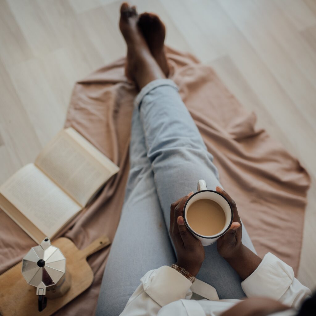 Legs of a woman holding a cup of coffee. An open notebook is beside her.